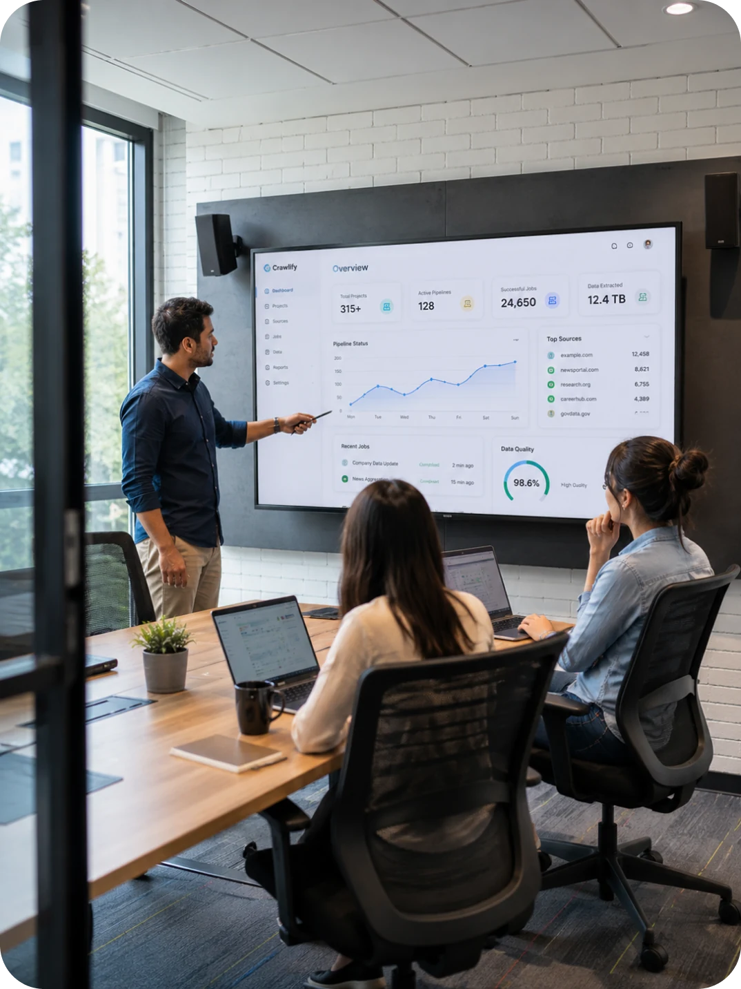 An engineer walking a seated team through performance dashboards on a wall display
