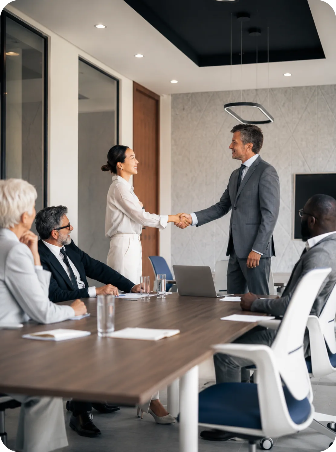 Two colleagues shaking hands across a boardroom table after agreeing a data partnership